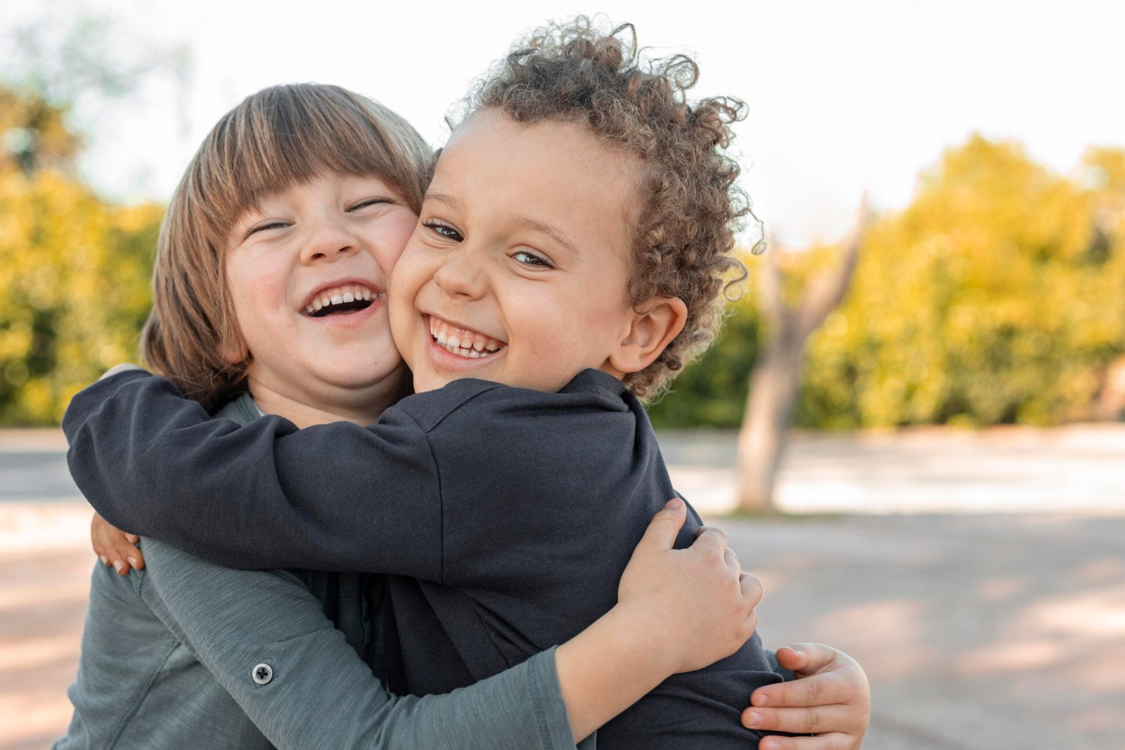 Uma imagem de dois irmãos, um mais velho e um mais novo, abraçados e sorrindo. O irmão mais velho é um menino de cabelos castanhos e olhos verdes, que veste uma camiseta azul e um short cinza. O irmão mais novo é um bebê de cabelos loiros e olhos azuis, que veste um macacão branco e um gorro vermelho. A imagem tem um fundo branco e um texto em rosa que diz: “Família e Relacionamentos: Como lidar com o ciúme do irmão mais velho”.